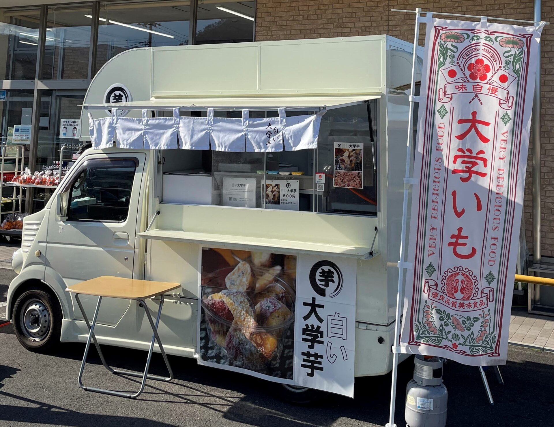 キッチンカーまる芋さんの外観です。白い車体、画像右側には「大学いも」と書かれたのぼりが立っています。